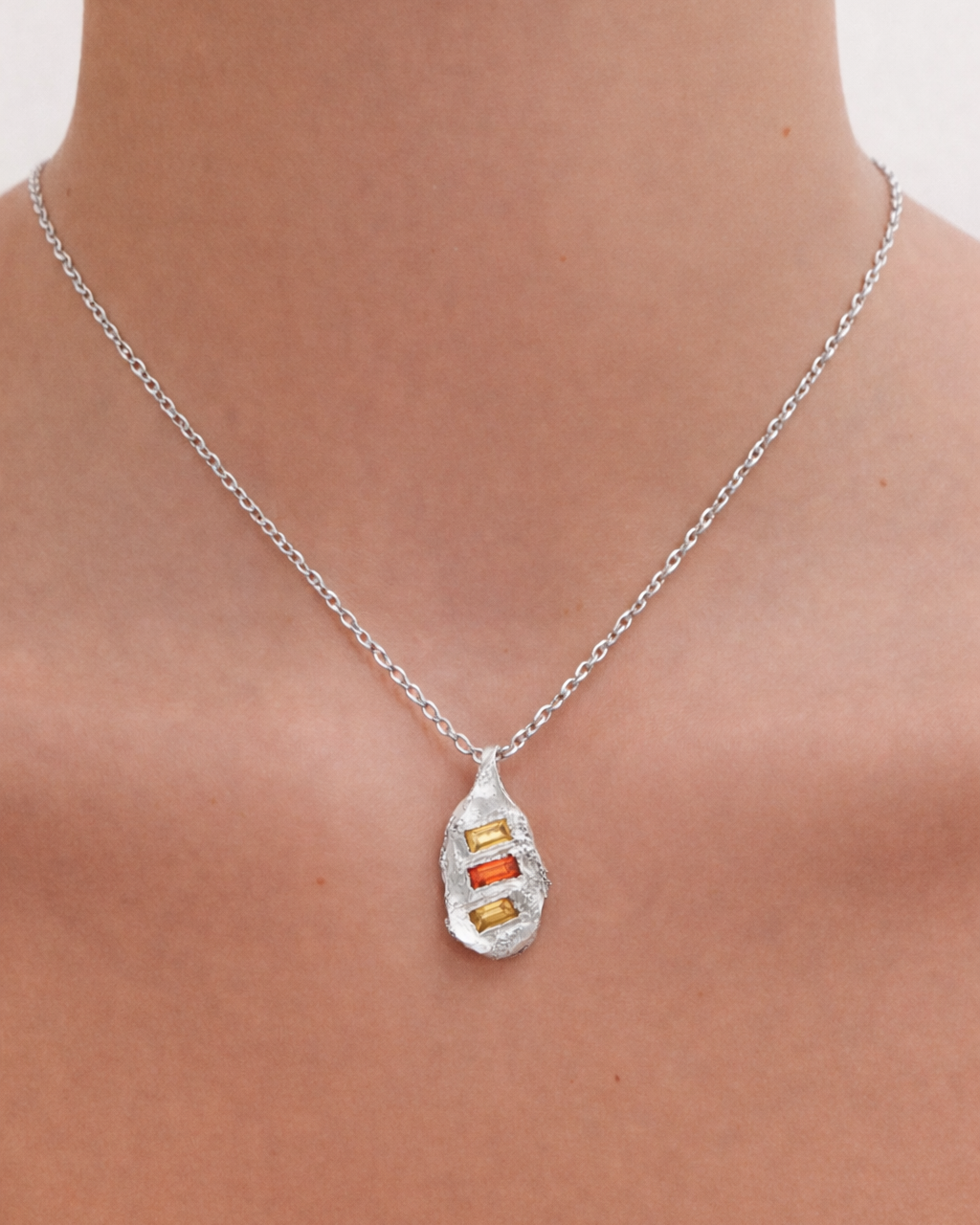 Silver necklace with a pendant on a person's neck against a neutral background