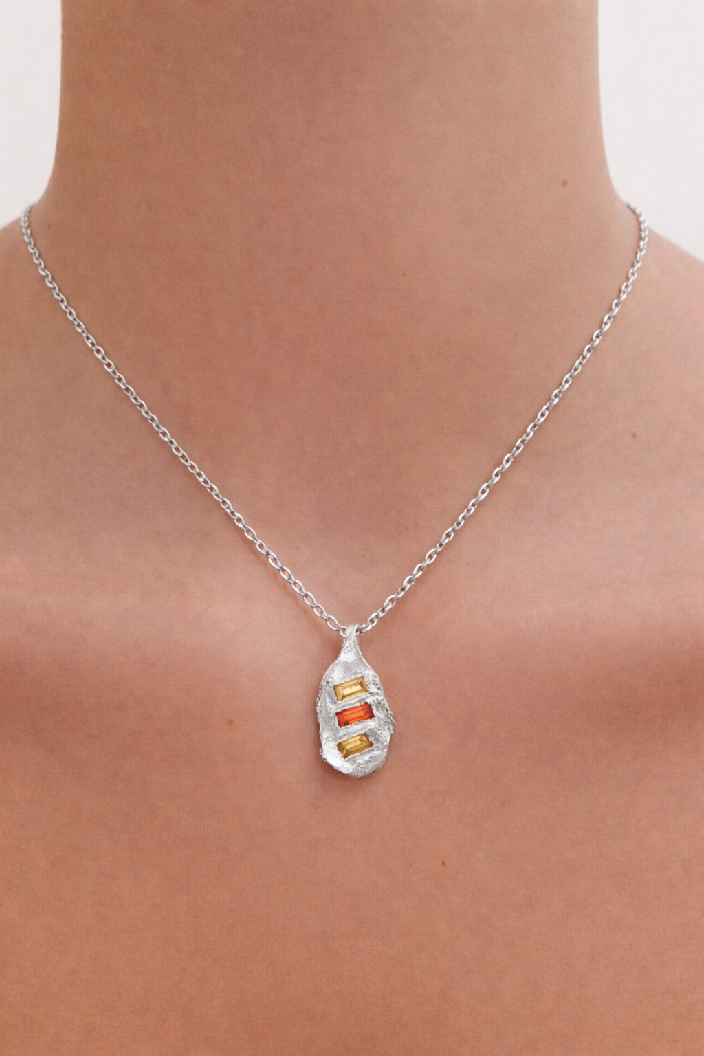 Silver necklace with a pendant on a person's neck against a neutral background