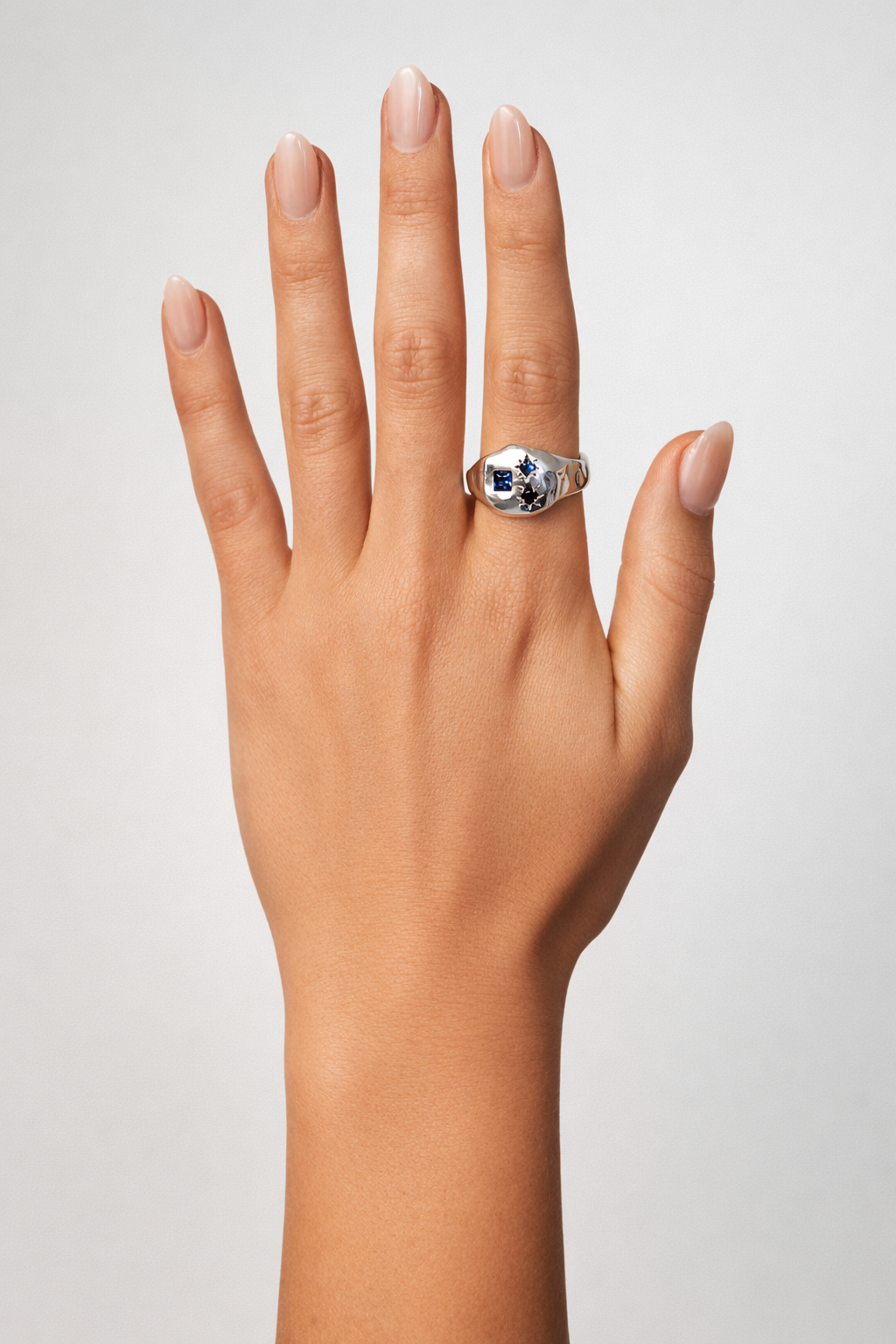 Hand wearing a ring with a blue gemstone on a neutral background